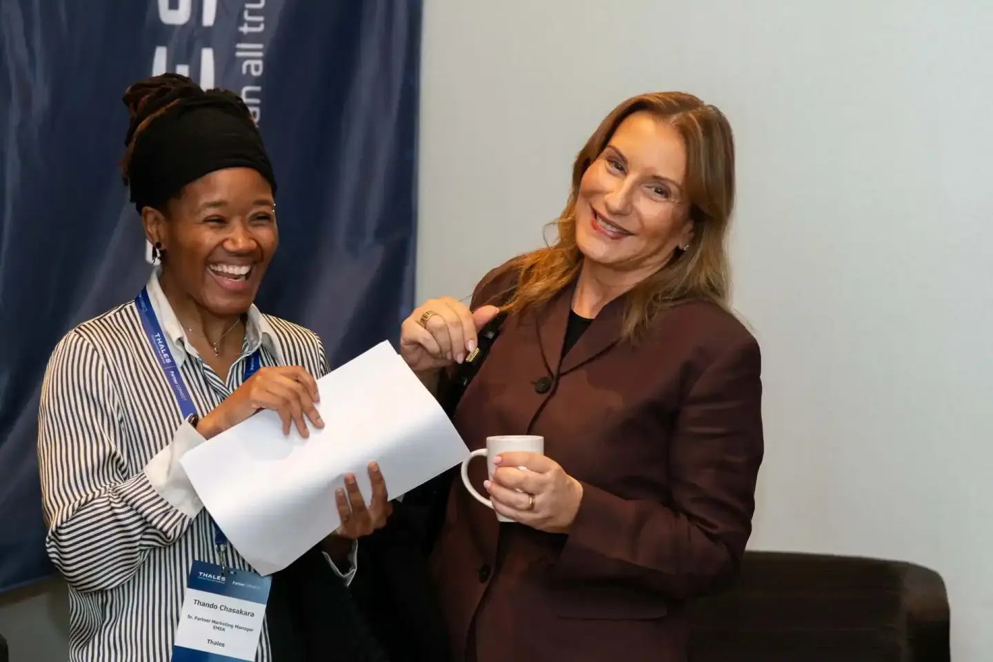 Zwei Frauen bei Thales Firmenevent Wien: Eine trägt Namensschildausweis und Streifenbluse, die andere in braunem Blazer hält 