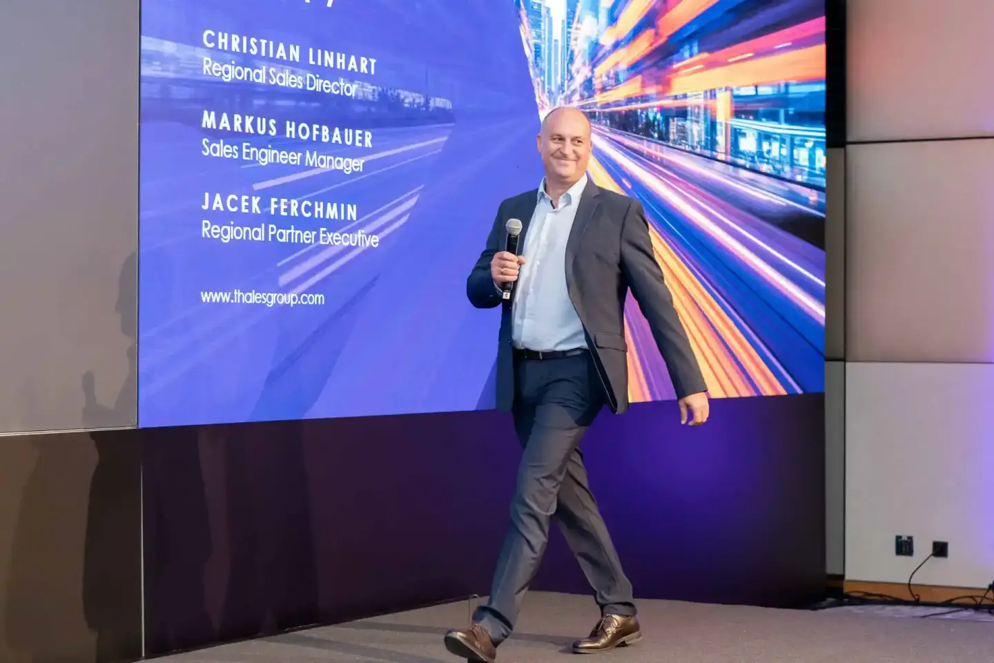 Geschäftsmann hält Präsentation auf Firmenevent Wien, im Hintergrund Bildschirm mit Thales-Mitarbeiterdaten