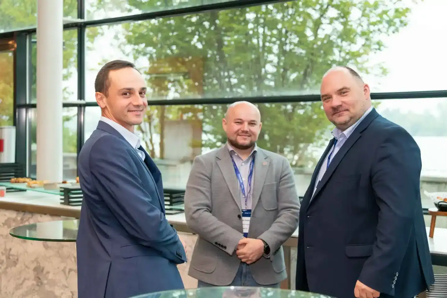 Drei Geschäftsmänner bei einem Firmenevent Wien – professionelle Handshake vor großem Fenster mit Waldblick
