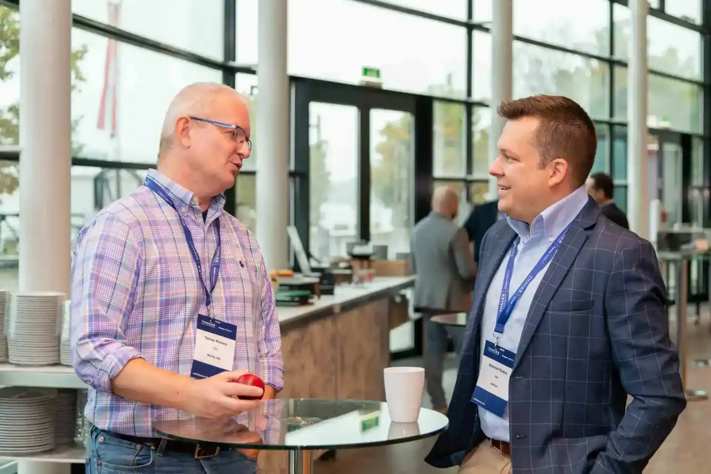 Zwei Geschäftsmänner im Gespräch auf einem Firmenevent Wien, beide tragen Namensschilder und halten Getränke