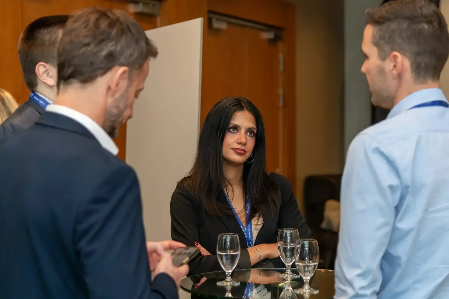Geschäftsfrau im Gespräch mit zwei Männern bei einem Firmenevent Wien, Networking an einem Tisch mit Wassergläsern
