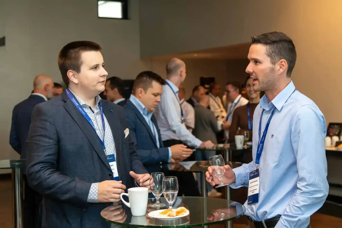 Zwei Geschäftsmänner mit Namensschildern bei einem Firmenevent Wien, unterhalten sich an einem Stehtisch mit Getränken