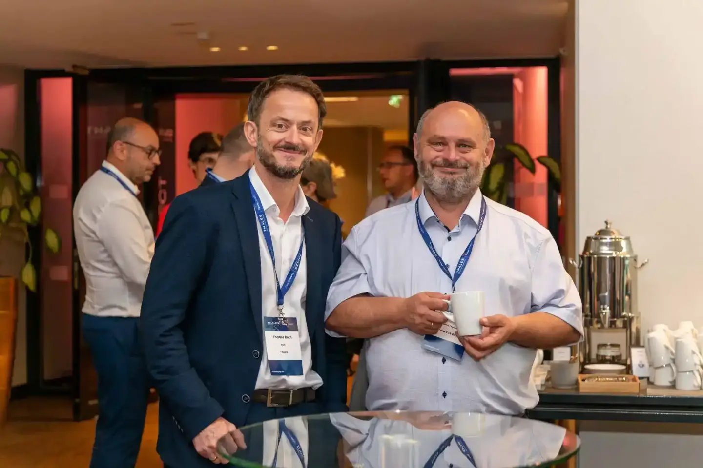 Zwei Geschäftsmänner mit Namensschildern beim Thales Firmenevent in Wien, einer hält eine Kaffeetasse