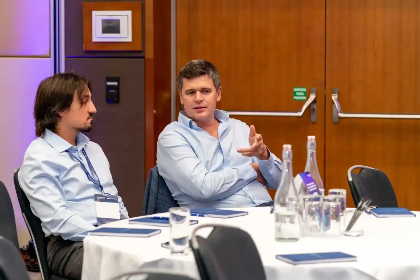 Zwei Geschäftsmänner in hellblauen Hemden bei einer Diskussionsrunde auf einem Firmenevent in Wien