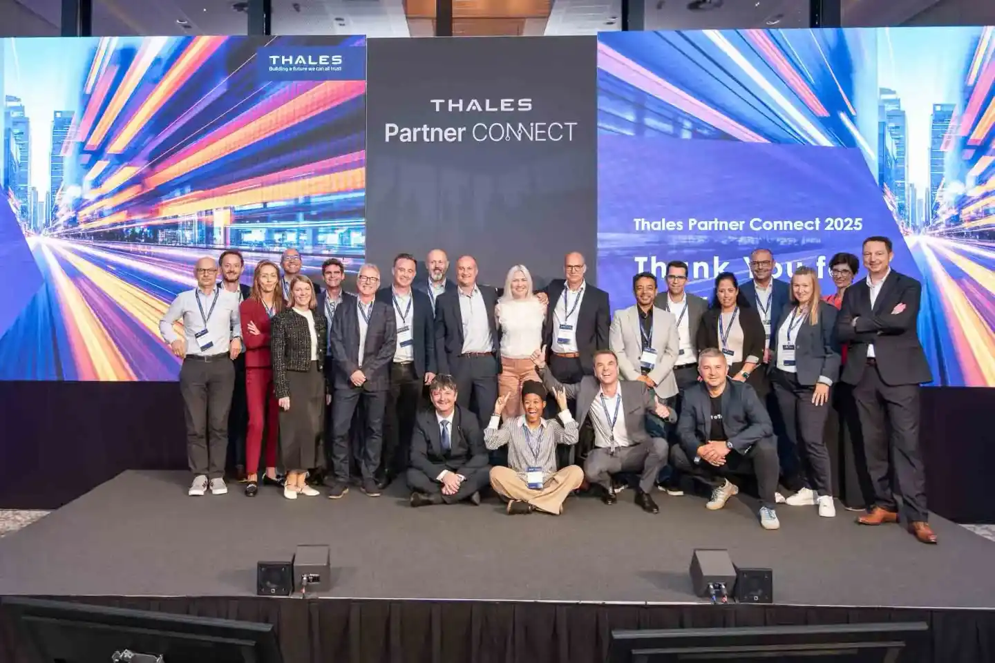 Teamfoto der Thales Partner Connect 2025 Konferenz mit etwa 25 Personen auf einer Bühne, professionelle Eventfotografie Wien