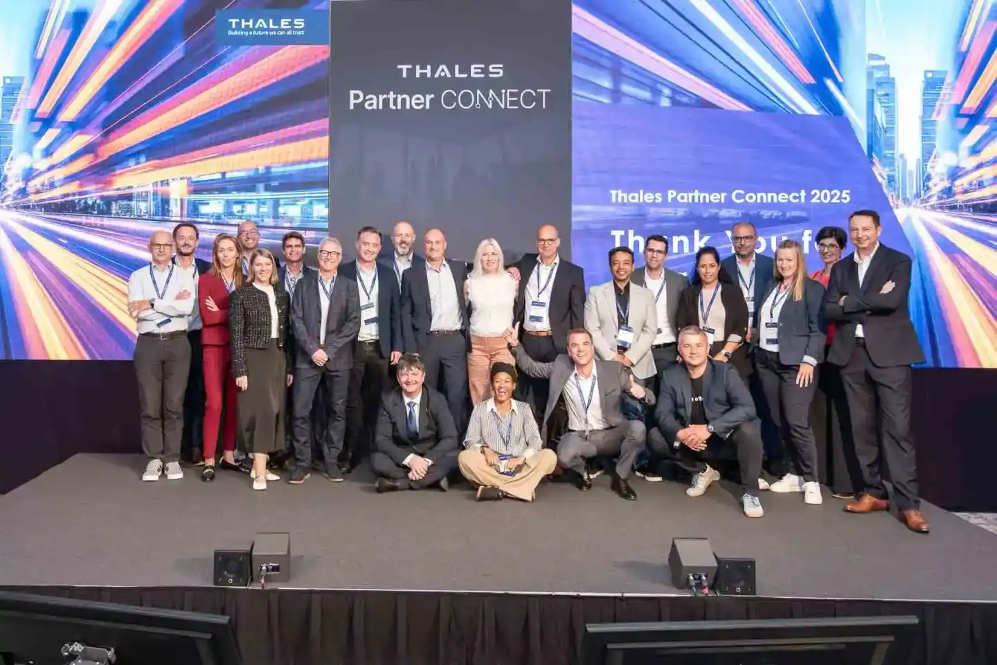 Gruppenfoto von etwa 25 Personen auf einer Bühne beim Thales Partner Connect 2025 Event - professionelle Eventfotografie Wien