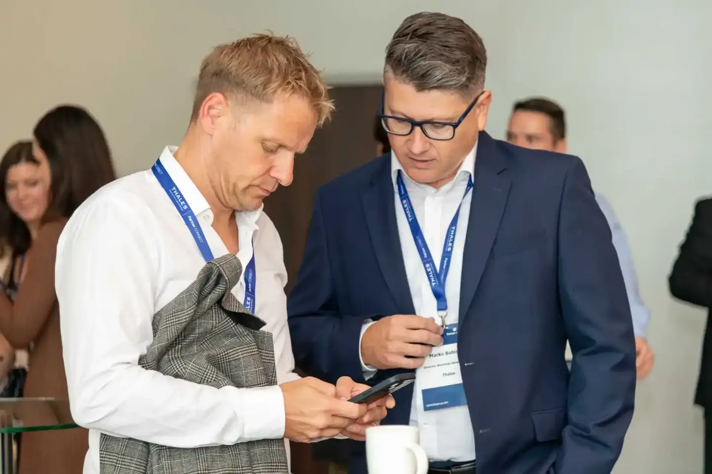 Zwei Geschäftsmänner mit Lanyards beim Firmenevent Wien, einer blickt auf ein Smartphone in seinen Händen