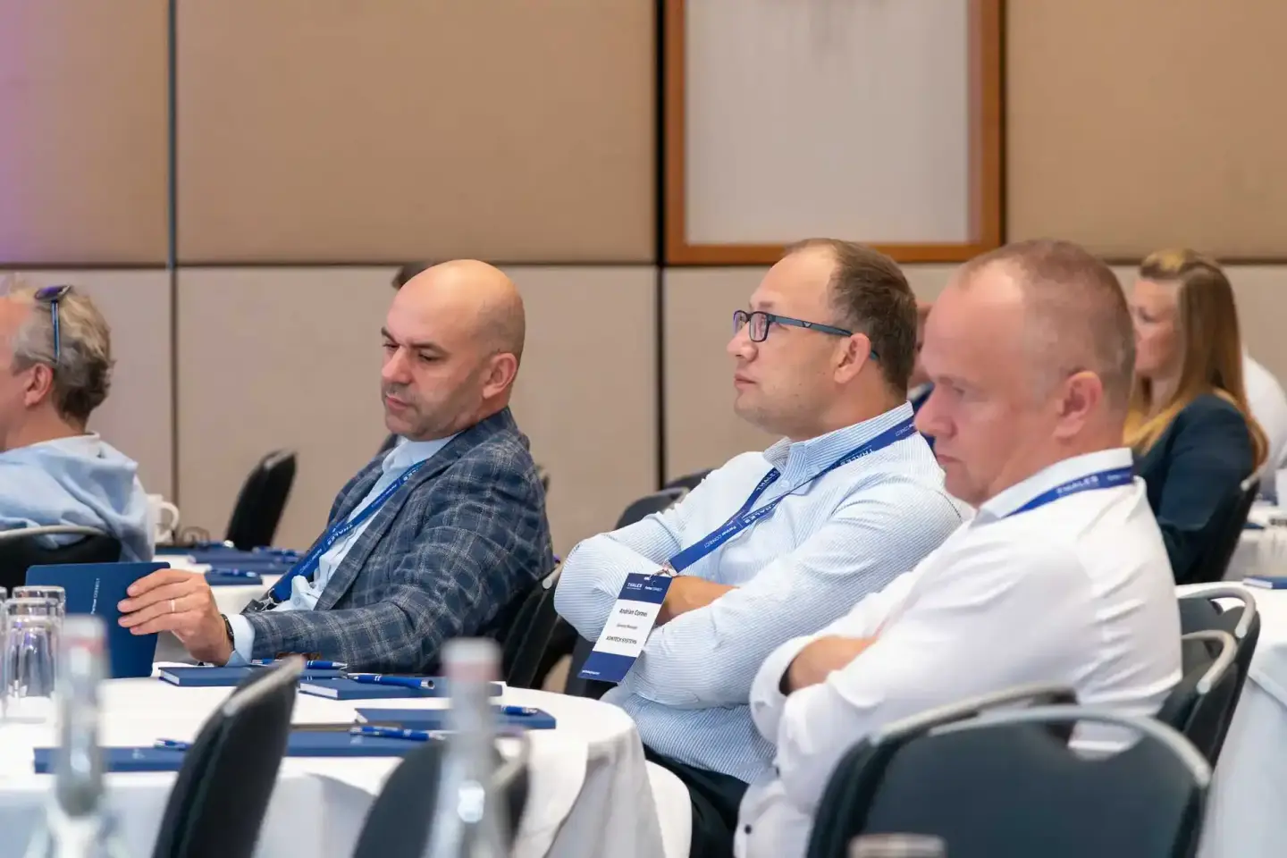 Geschäftsmänner in Business-Kleidung mit Namensschildern sitzen aufmerksam bei einem Firmenevent Wien an einem Konferenztisch