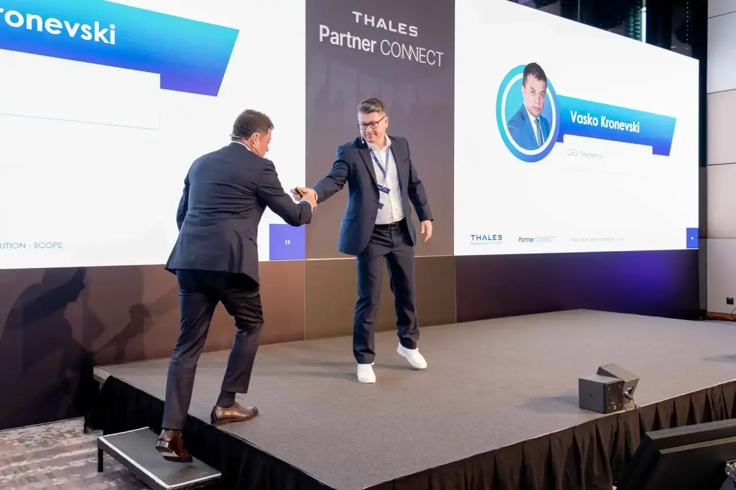 Zwei Geschäftsmänner schütteln sich die Hand auf der Bühne bei der Thales Partner Connect Veranstaltung, Eventfotograf Wien d