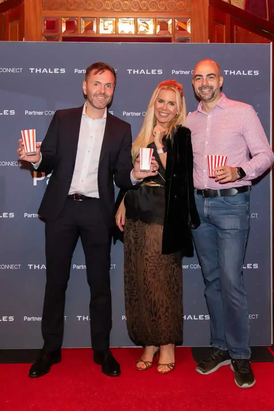 Drei Personen posieren mit Popcorn-Bechern vor Thales-Backdrop auf rotem Teppich bei Firmenevent Wien