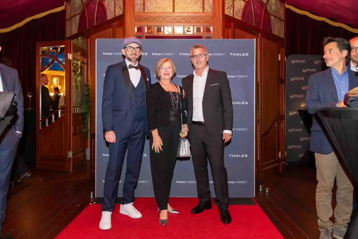 Drei elegant gekleidete Personen posieren auf dem roten Teppich bei einem Firmenevent Wien vor einer Thales-Backdrop.