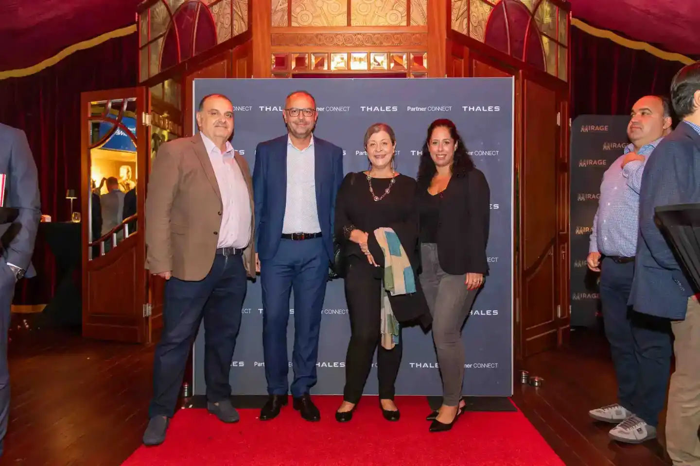 Vier Geschäftspersonen posieren vor einer Thales Partner Connect Backdrop auf dem roten Teppich eines Wiener Firmenevent