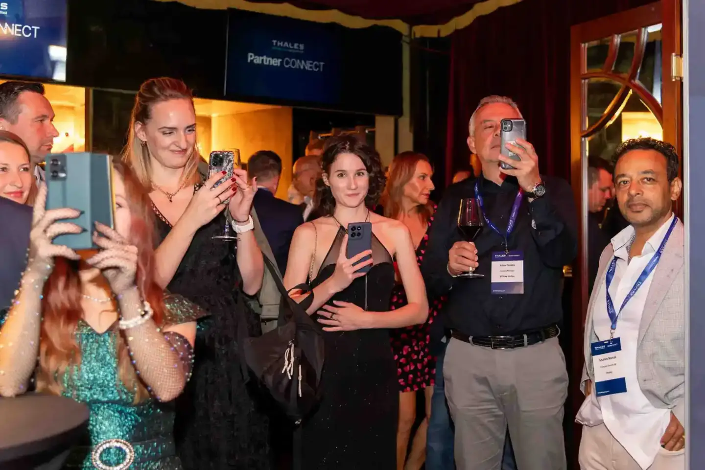 Gäste beim Thales Partner Connect Event in Wien dokumentieren das Firmenevent mit Smartphones und Getränken