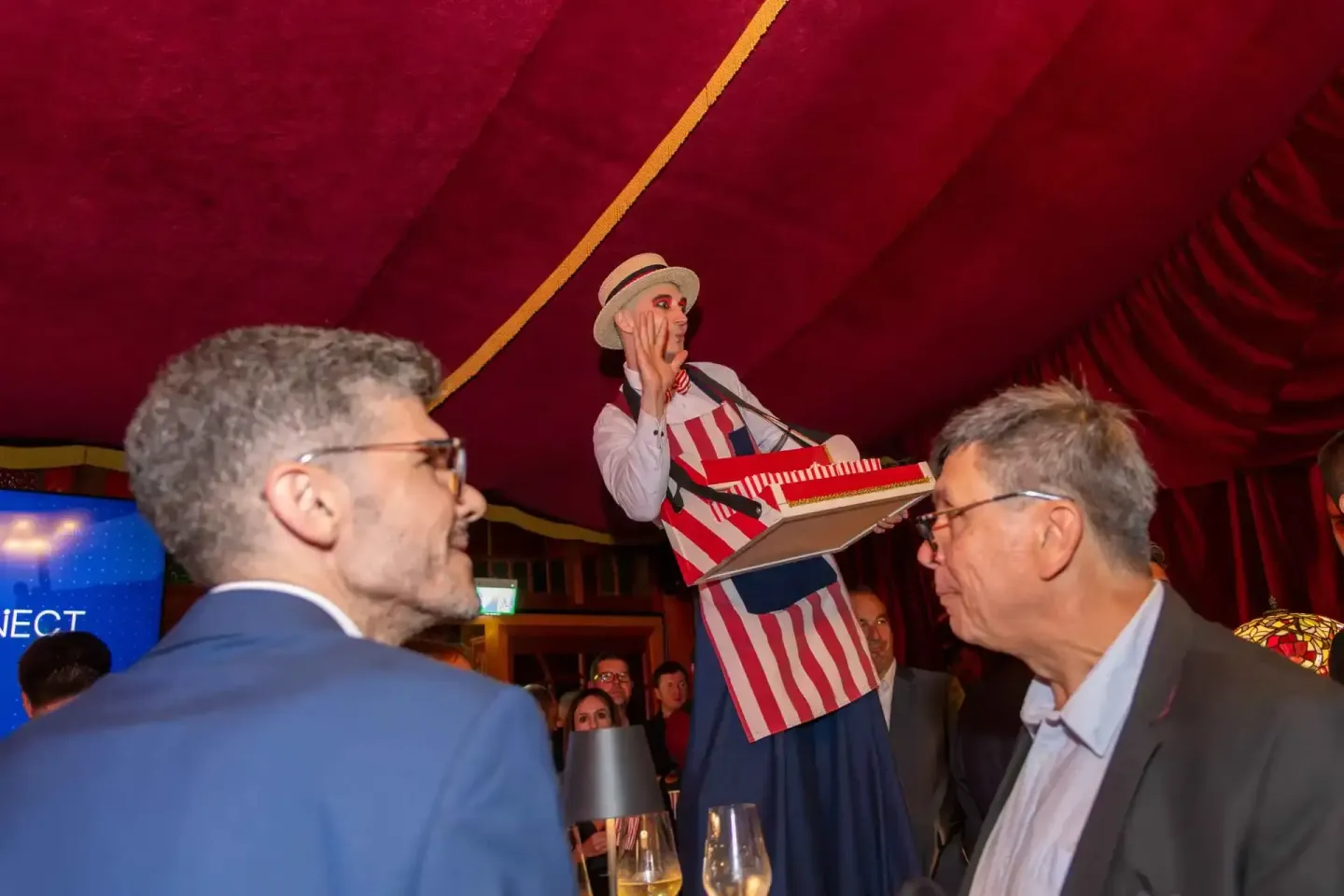 Eventfotograf Wien dokumentiert Firmenevent mit Zirkusperformer in rotem Zelt und Gästen in Business-Kleidung
