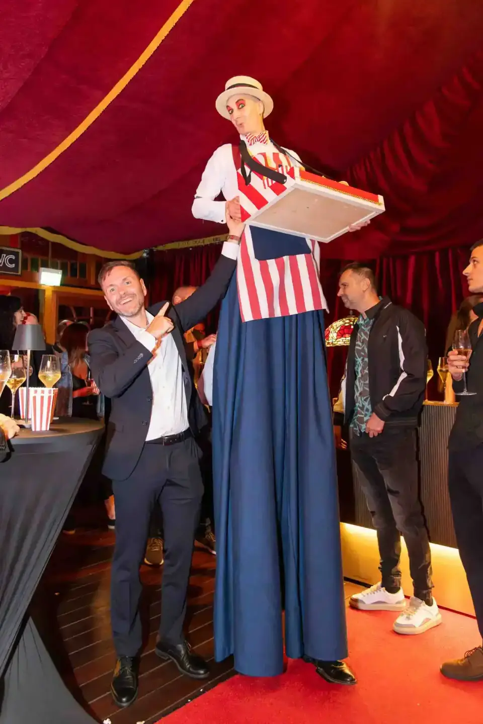 Eventfotograf Wien dokumentiert Firmenevent mit Stelzenläufer in Zirkuskostüm auf rotem Teppich unter rotem Zelt