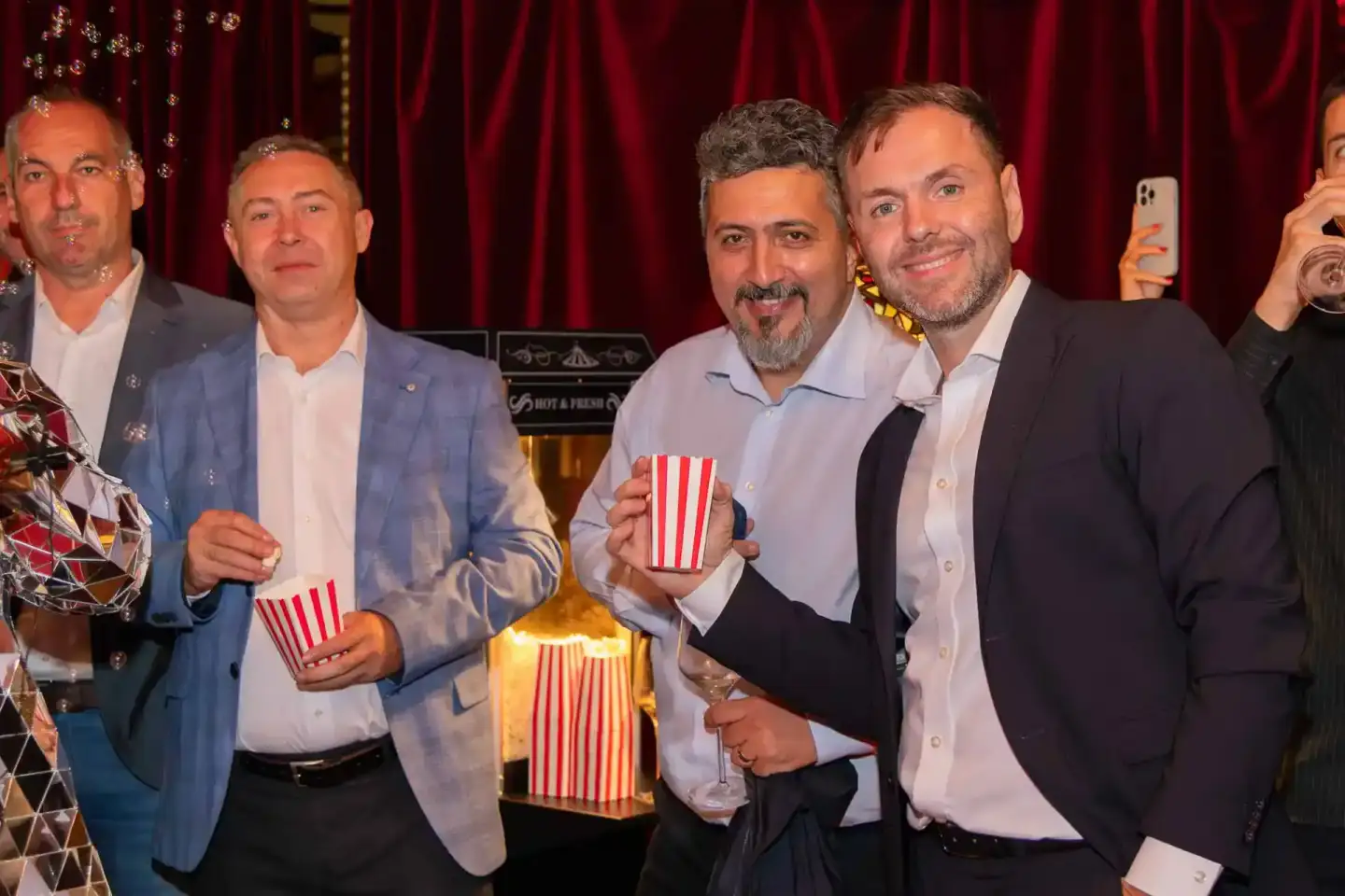 Vier Geschäftsmänner mit Popcorn-Bechern posieren vor rotem Vorhang bei einem Firmenevent Wien