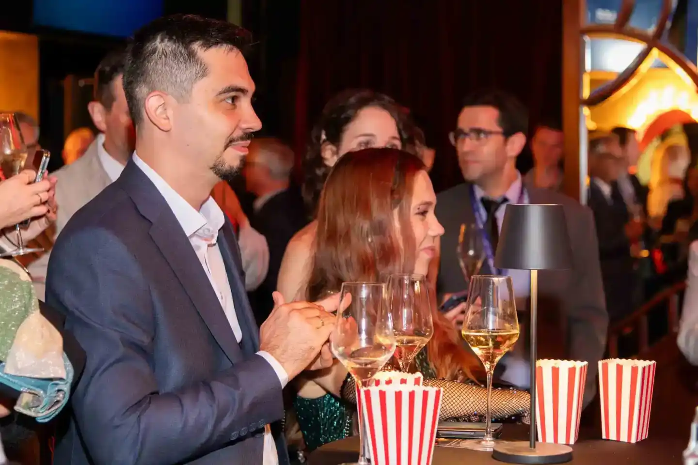 Elegante Eventfotografie Wien: Geschäftsmann im dunklen Anzug genießt Veranstaltung mit Wein und Popcorn neben Frau in grünem