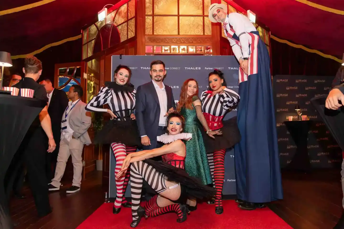 Eventfotografie Wien: Gruppe von Personen in bunten Zirkus-Kostümen posiert vor Thales-Backdrop auf rotem Teppich