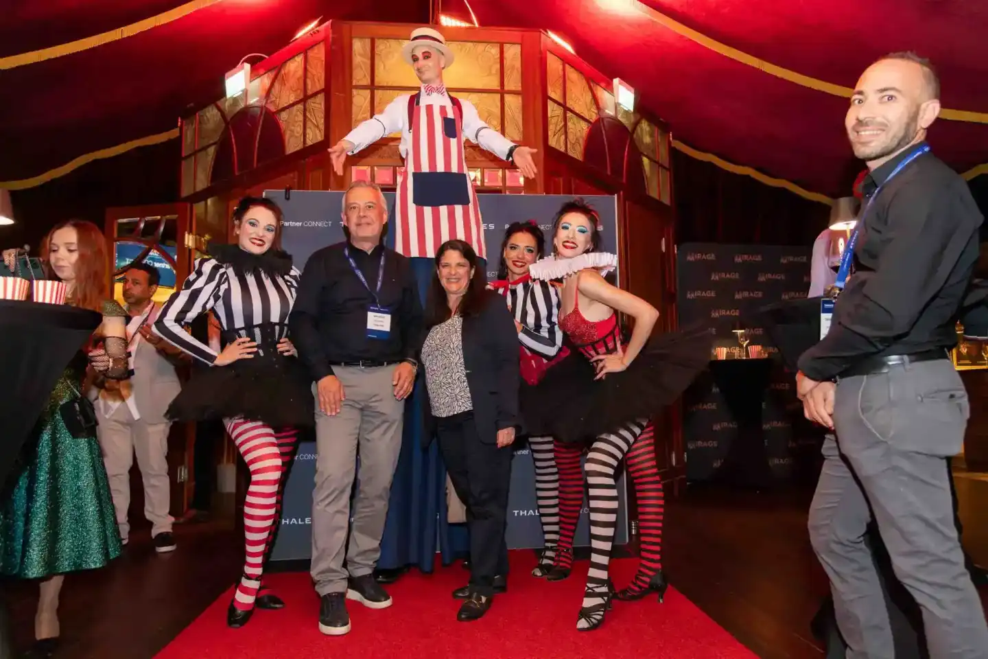 Eventfotografie Wien: Gruppe von Personen in Zirkuskostümen posiert auf rotem Teppich vor Zirkuszelt-Dekoration beim Thales F