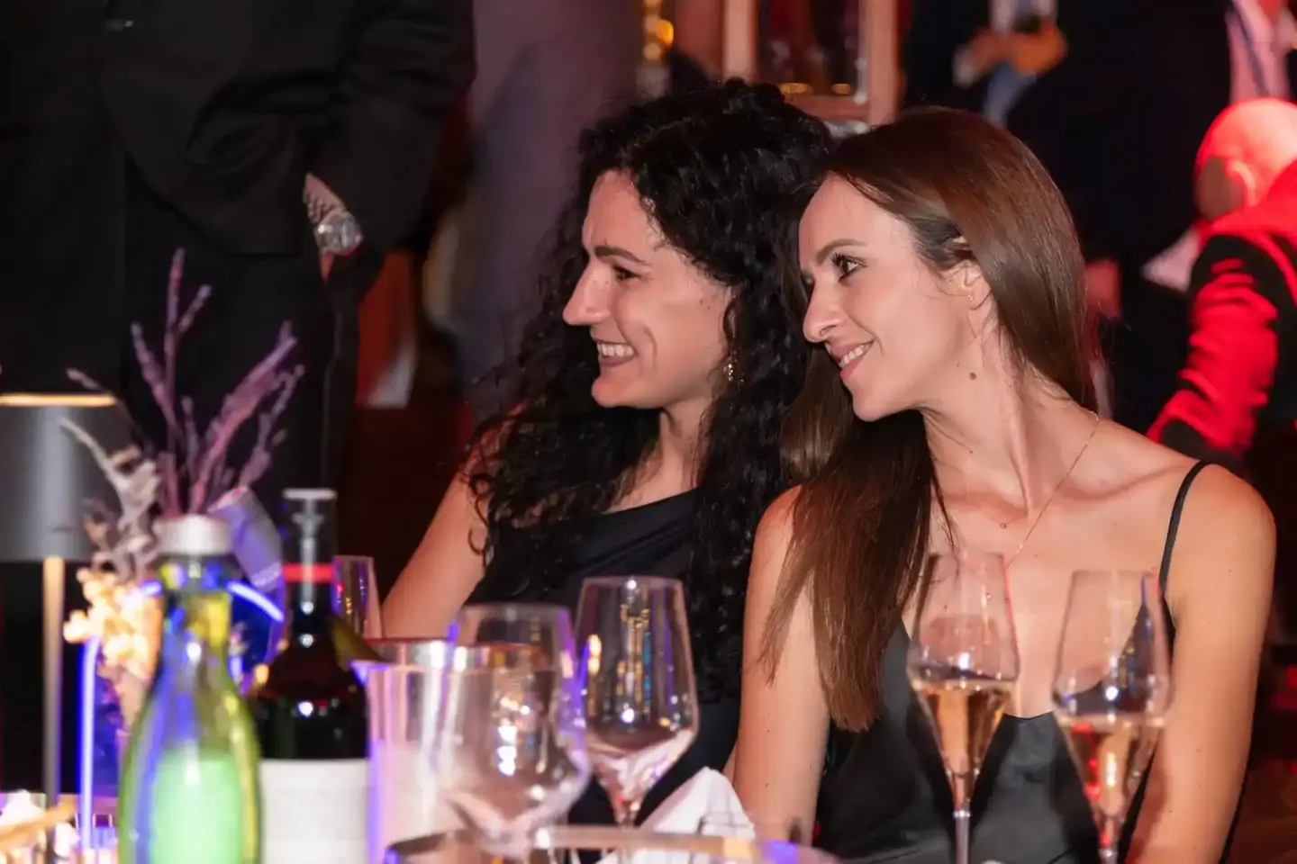 Zwei Frauen in eleganten schwarzen Kleidern genießen ein Firmenevent in Wien mit Sektgläsern und festlicher Tischdekoration