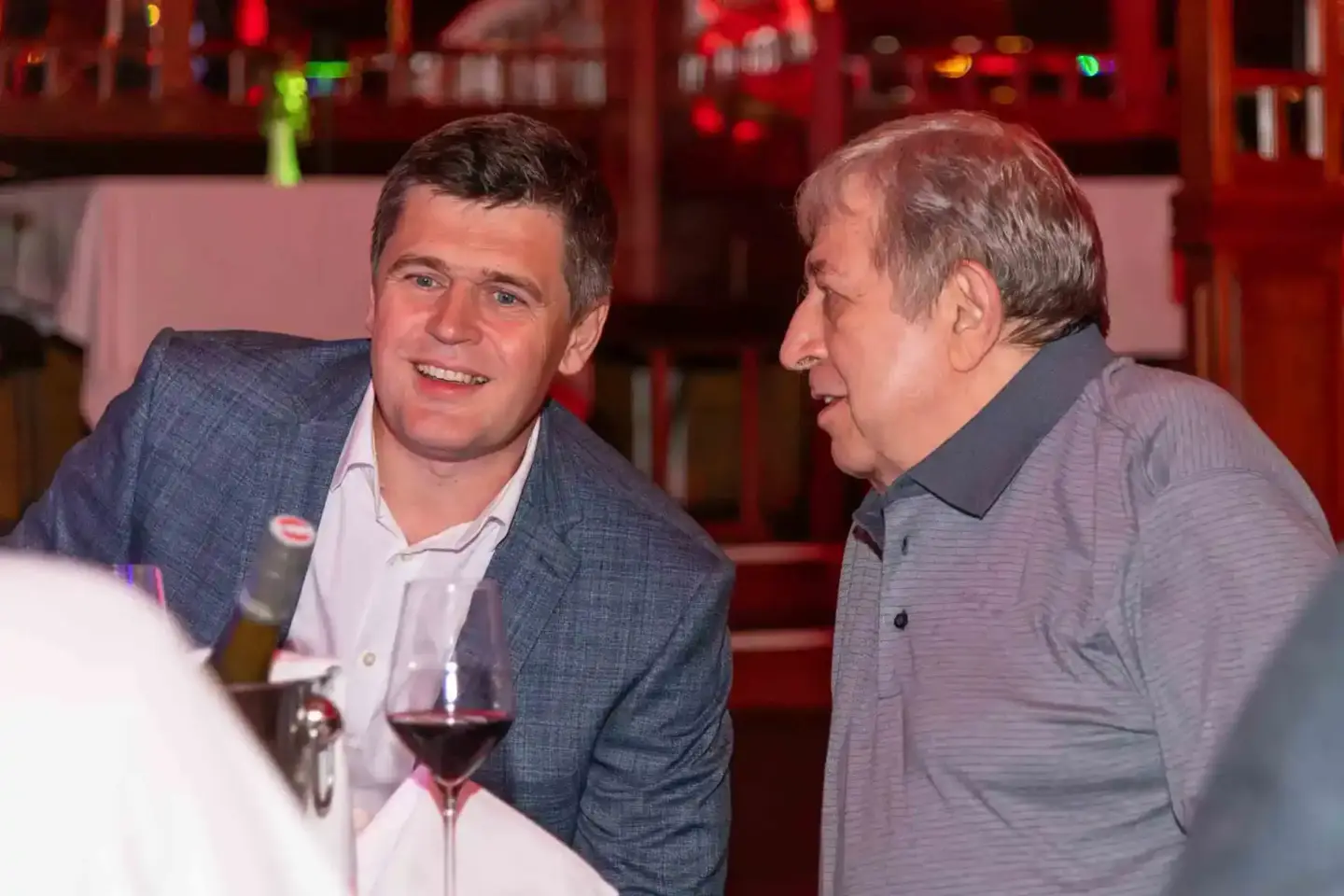 Zwei Männer im Gespräch bei einem Firmenevent in Wien, mit Weingläsern und roter Beleuchtung im Hintergrund