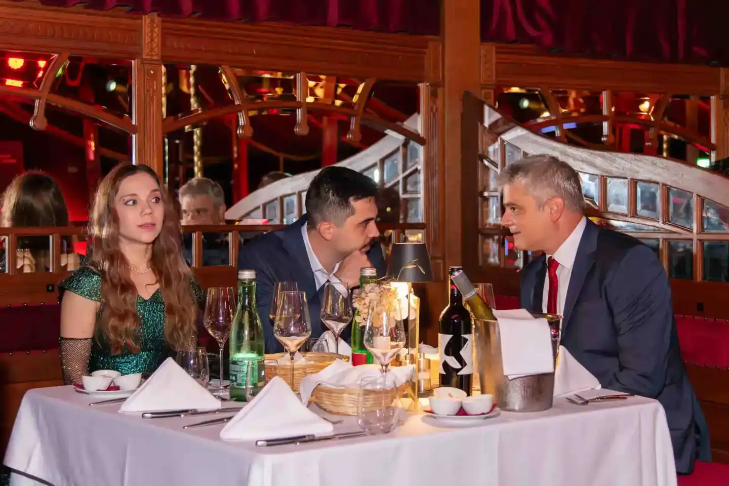 Elegantes Firmenevent Wien in rotem Ambiente: Drei Personen an gedecktem Tisch mit Weingläsern und Besteck, professionelle Ev