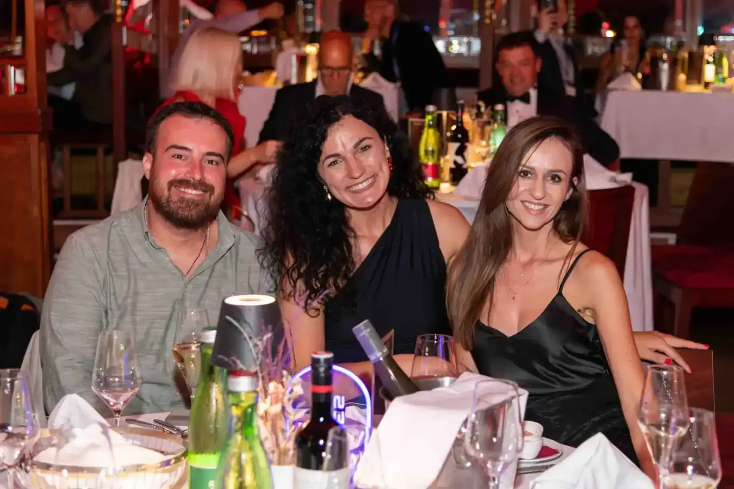 Drei lachende Gäste beim Thales Firmenevent in Wien sitzen an einem gedeckten Tisch mit Getränken