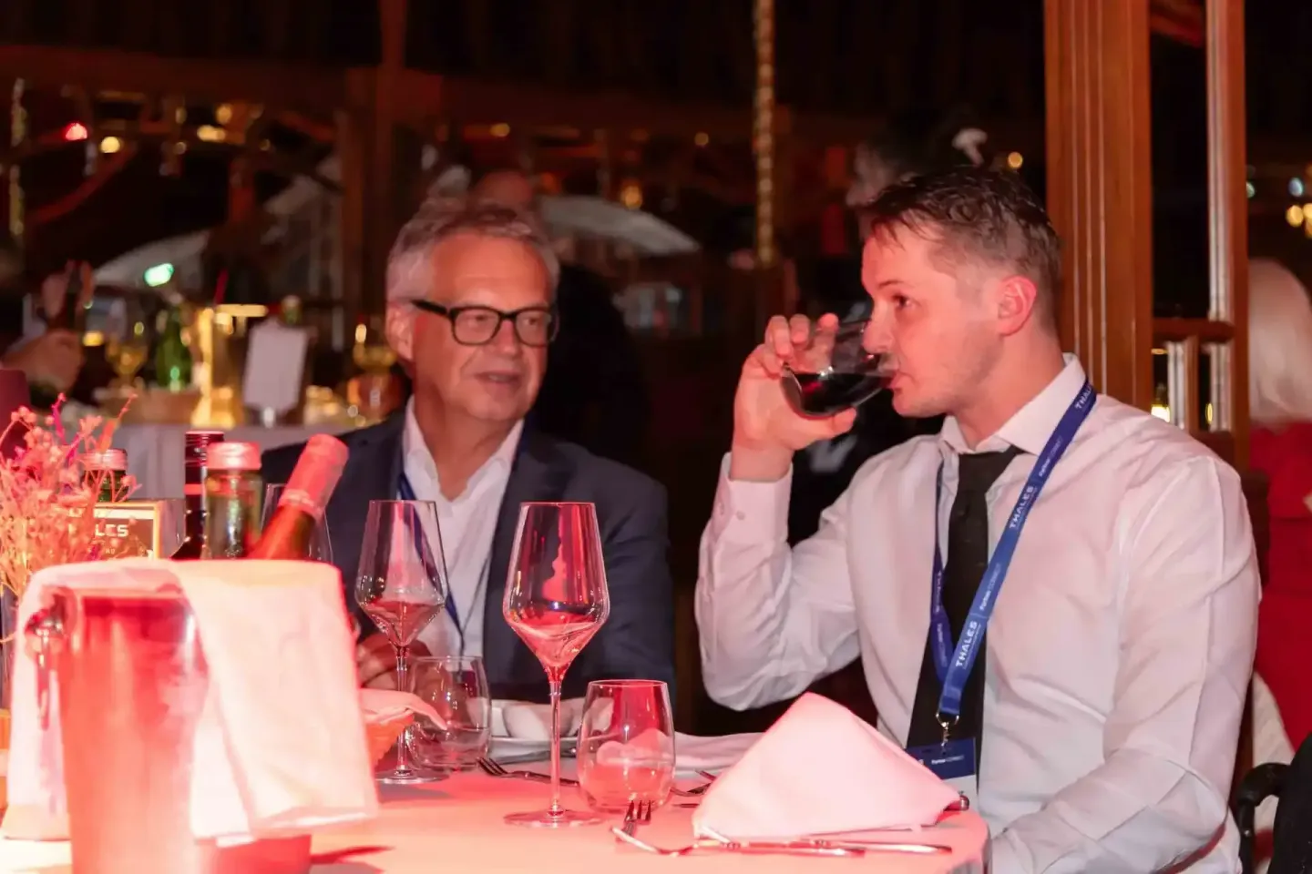 Zwei Geschäftsmänner beim Networking auf einem Firmenevent in Wien, einer trinkt aus einem Weinglas