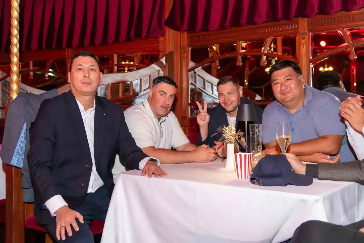 Vier Männer sitzen an einem Tisch beim Thales Firmenevent Wien, lächeln in die Kamera, mit Champagner und Popcorn als Dekorat