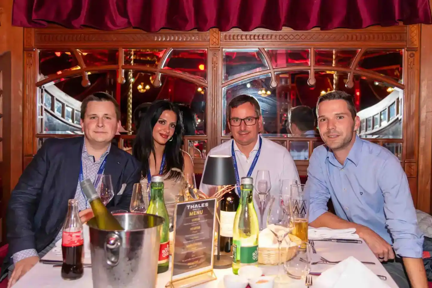 Vier Geschäftsleute beim Thales Firmenevent in Wien, sitzen an gedecktem Tisch mit Getränken und lächeln in die Kamera