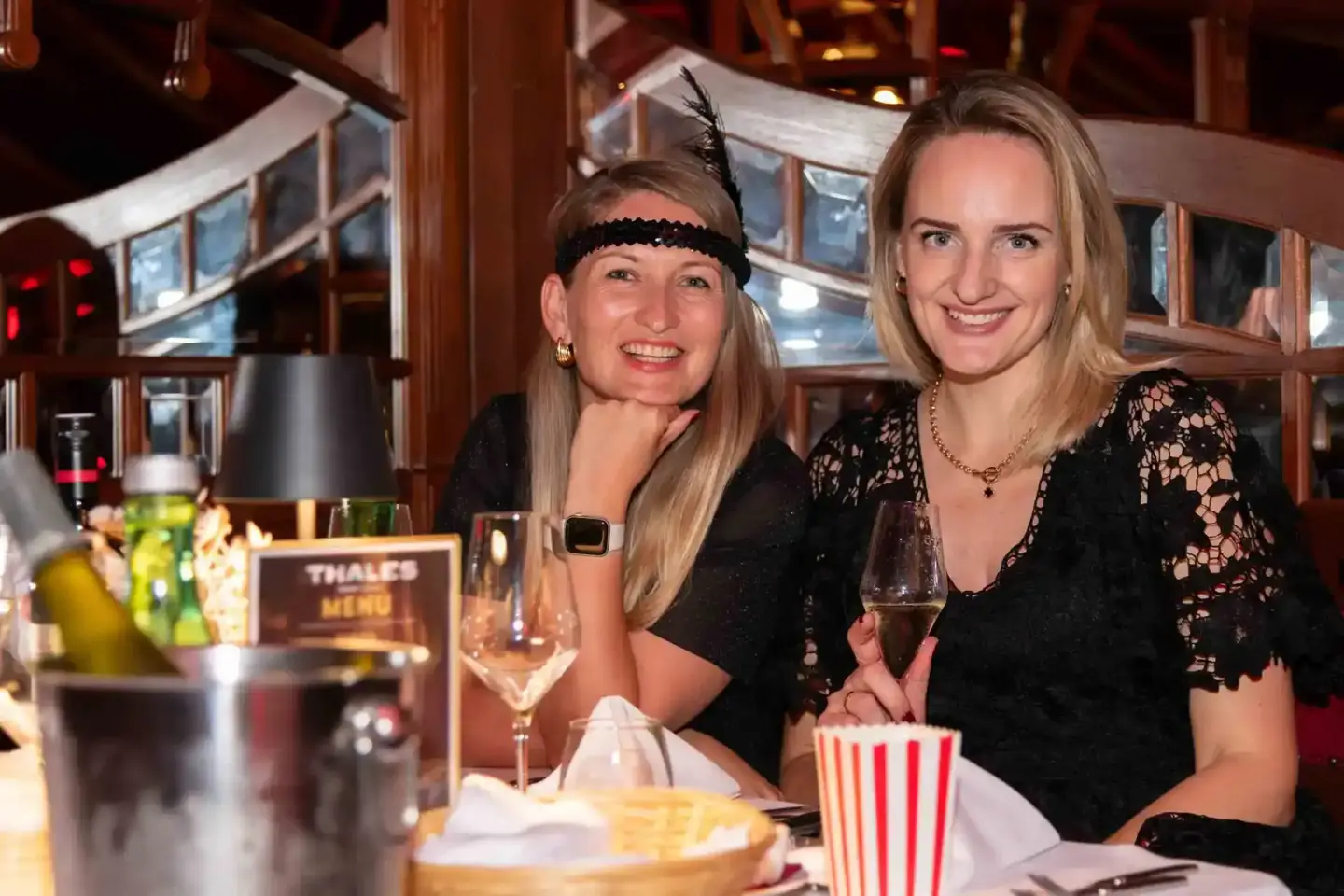 Zwei Frauen in eleganter schwarzer Kleidung beim Thales Firmenevent in Wien, lachend mit Champagner und Popcorn