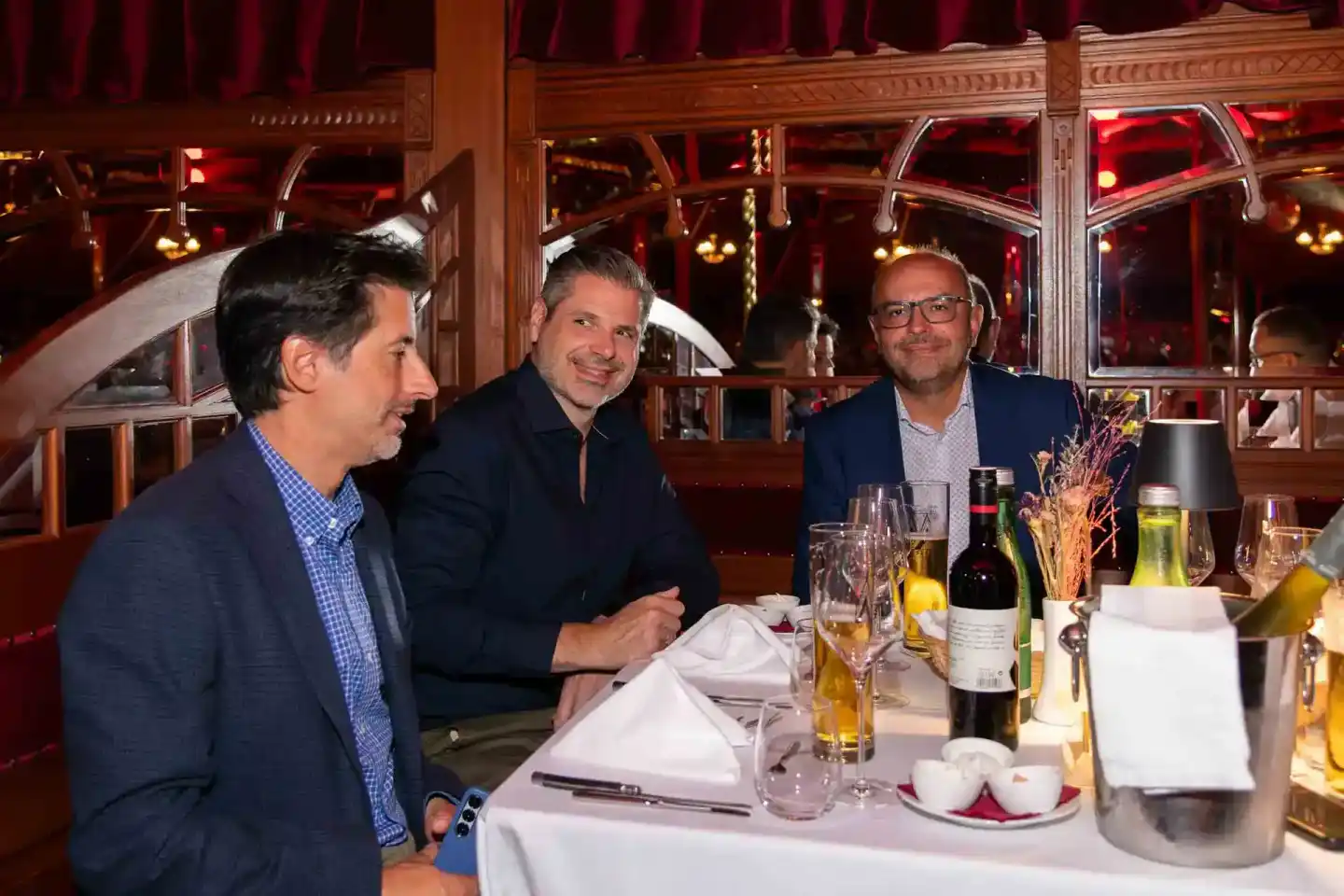 Drei Geschäftsmänner in eleganter Kleidung beim Networking bei einem Firmenevent Wien an einem gedeckten Tisch mit Wein