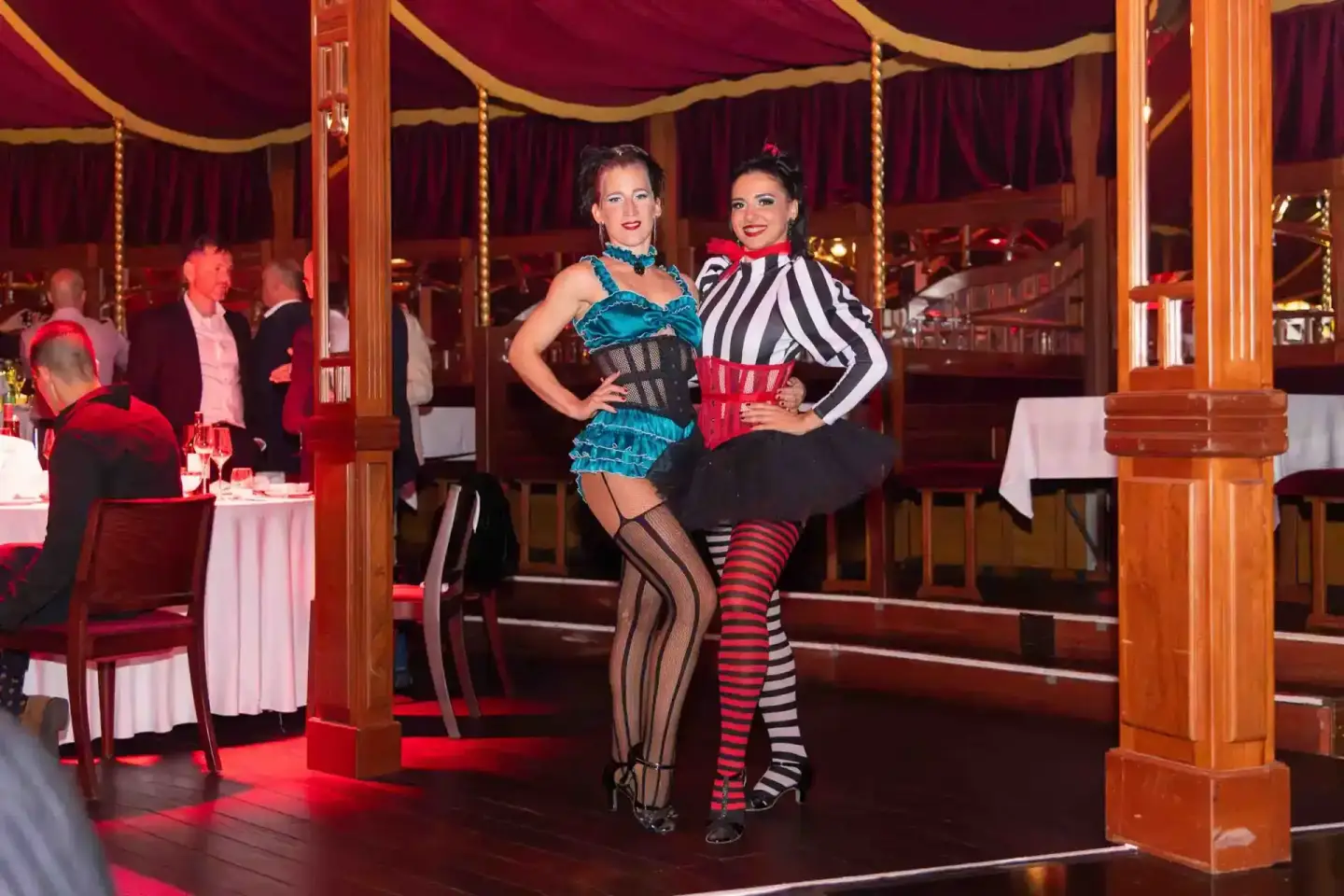 Zwei Performerinnen in glitzernden Kostümen bei Eventfotografie Wien auf einer Bühne mit rotem Licht und burgundy Vorhängen