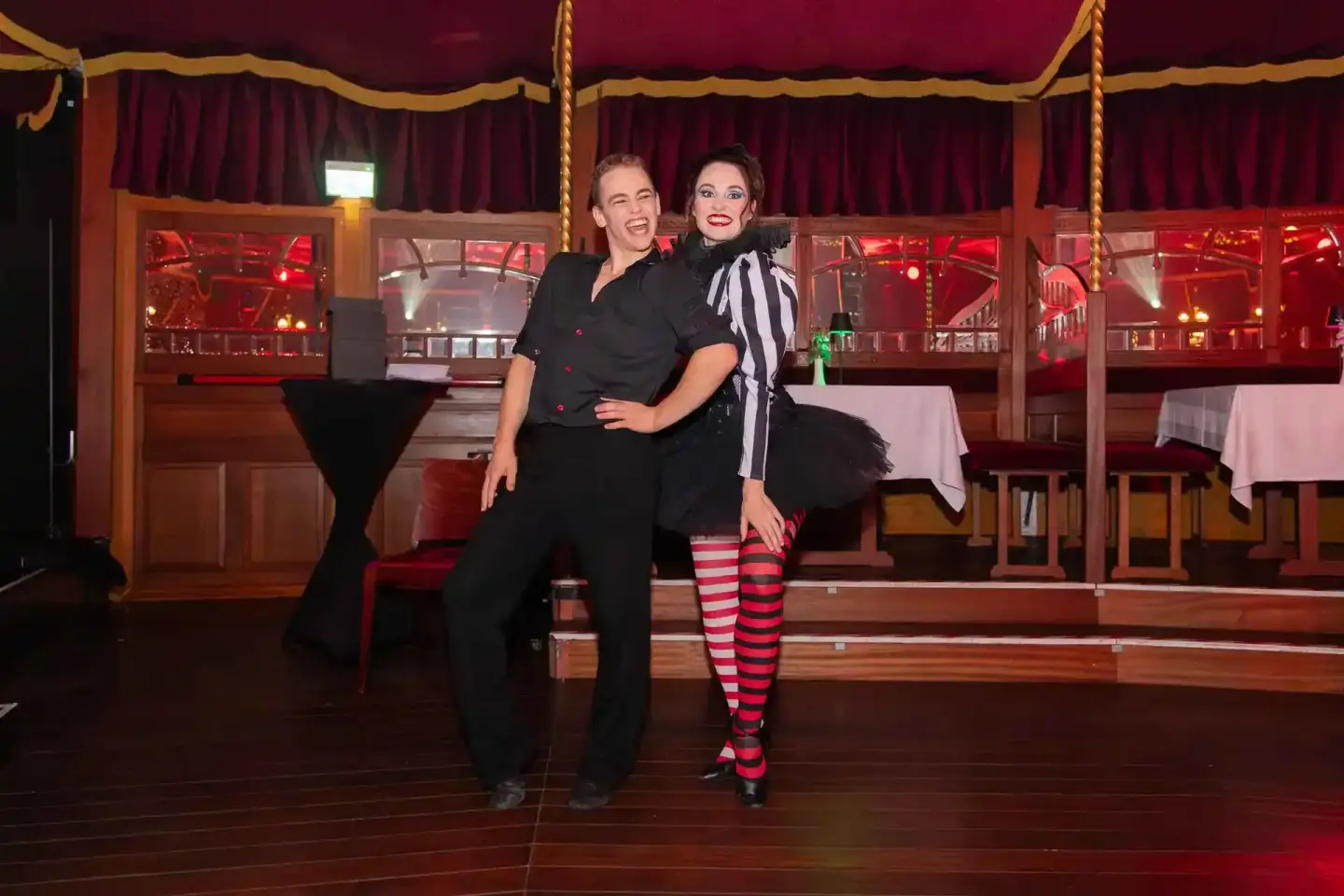 Zwei Frauen in eleganten schwarzen Outfits posieren lachend auf einer Bühne mit rotem Samtvorhang – professionelle Eventfotog