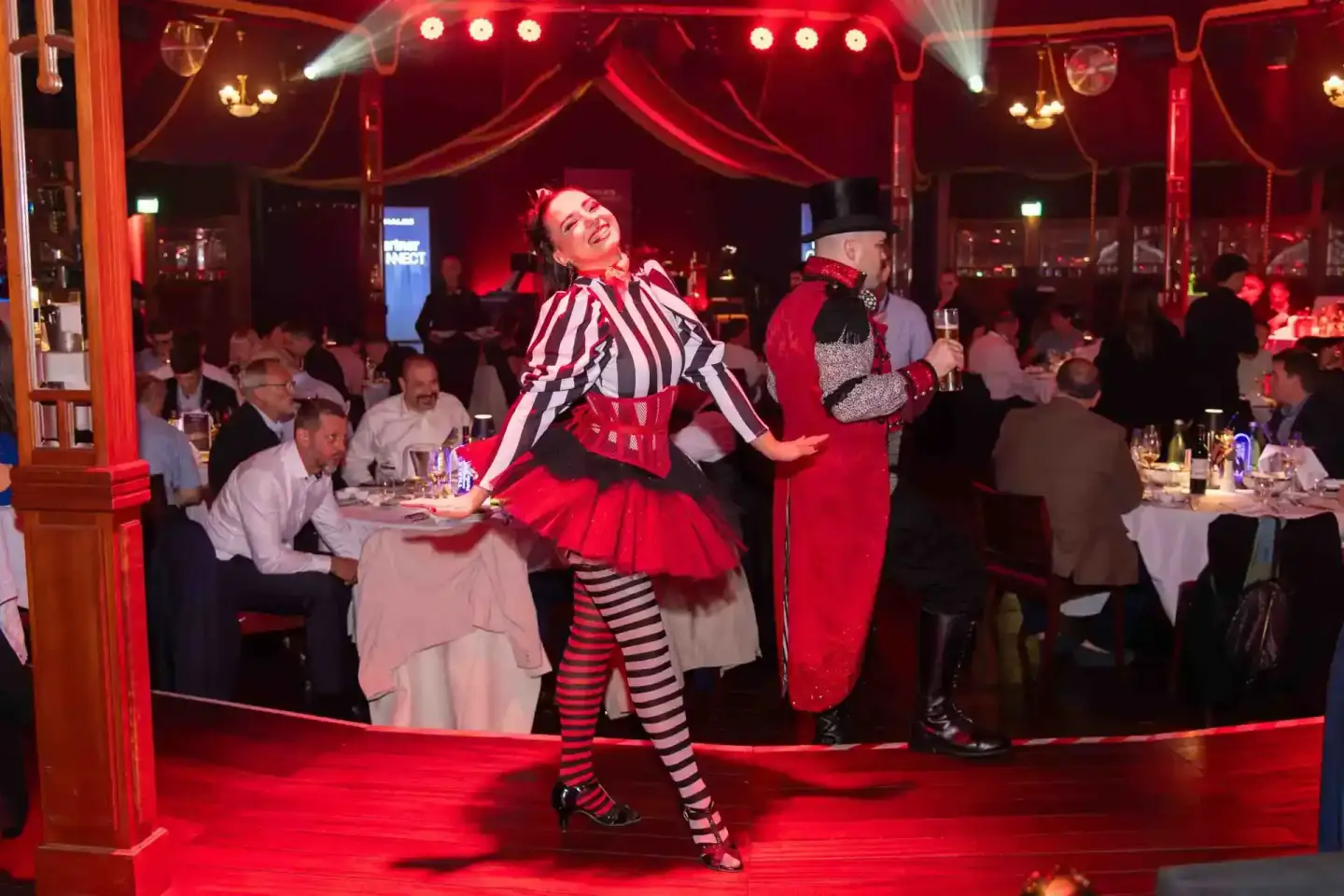 Eventfotografie Wien: Artistin in rotem Kostüm mit Zylinder performt vor Gästen in eleganter Veranstaltungshalle
