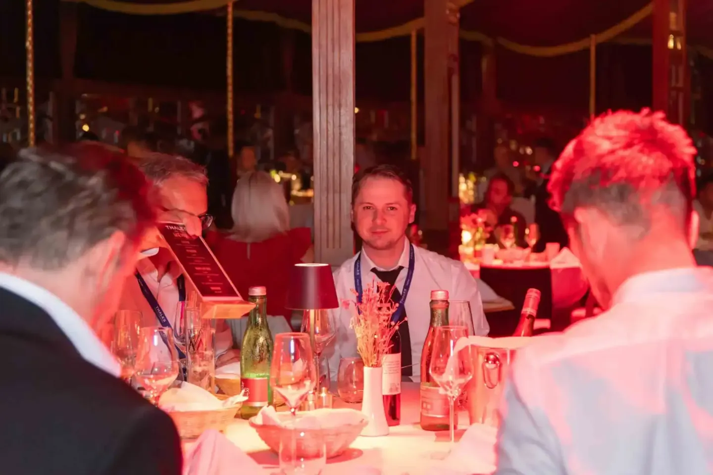 Eventfotograf Wien dokumentiert Gala-Dinner mit Geschäftsgästen an elegant gedecktem Tisch unter roter Beleuchtung