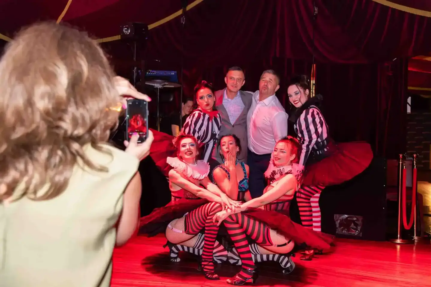 Eventfotograf dokumentiert Cabaret-Performance: Showgirls in roten Kostümen mit Gästen beim Firmenevent in Wien