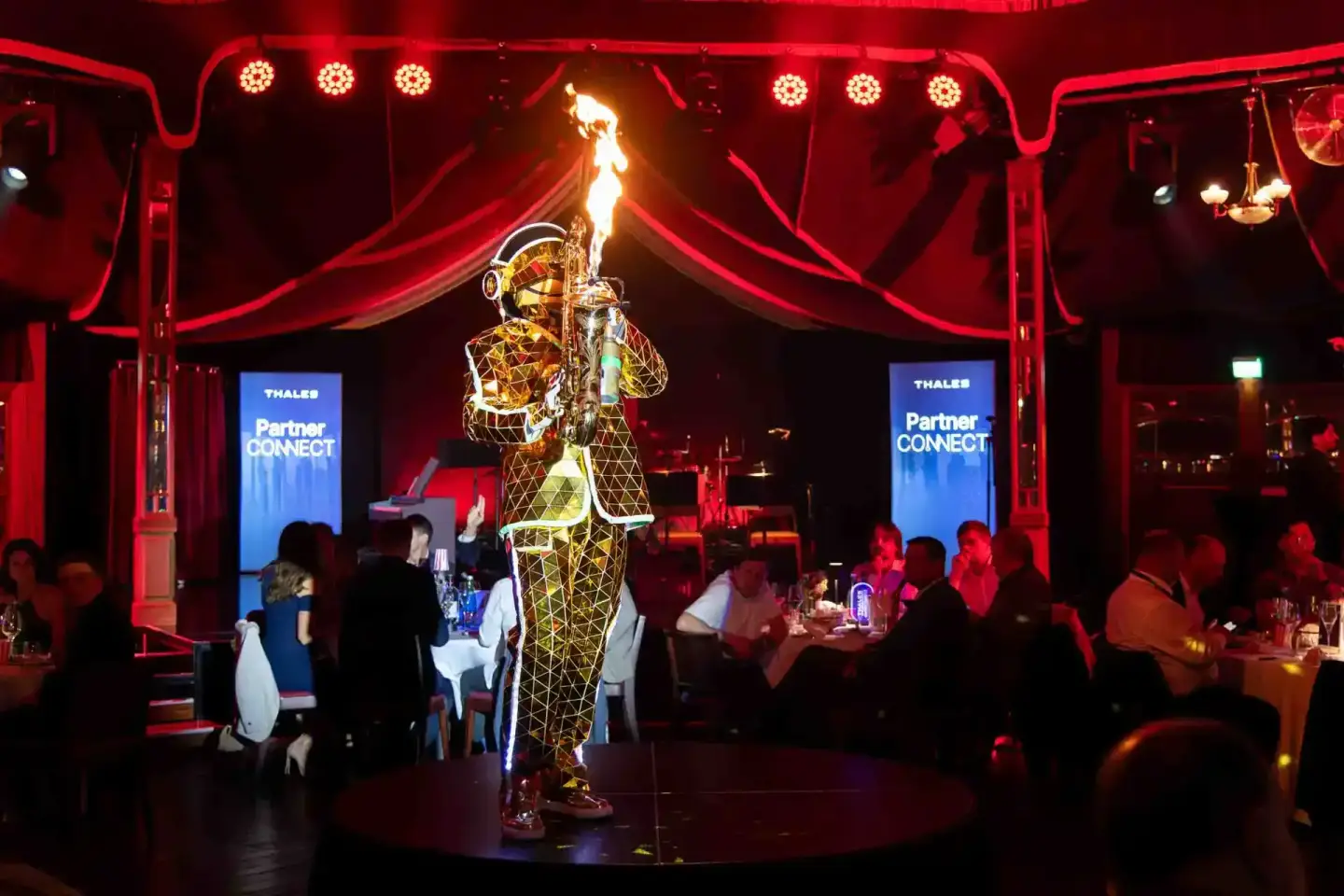 Flammenwerfer-Performer auf der Bühne der Thales Partner Connect Veranstaltung in Wien, umgeben von Gästen und roter Bühnenbe