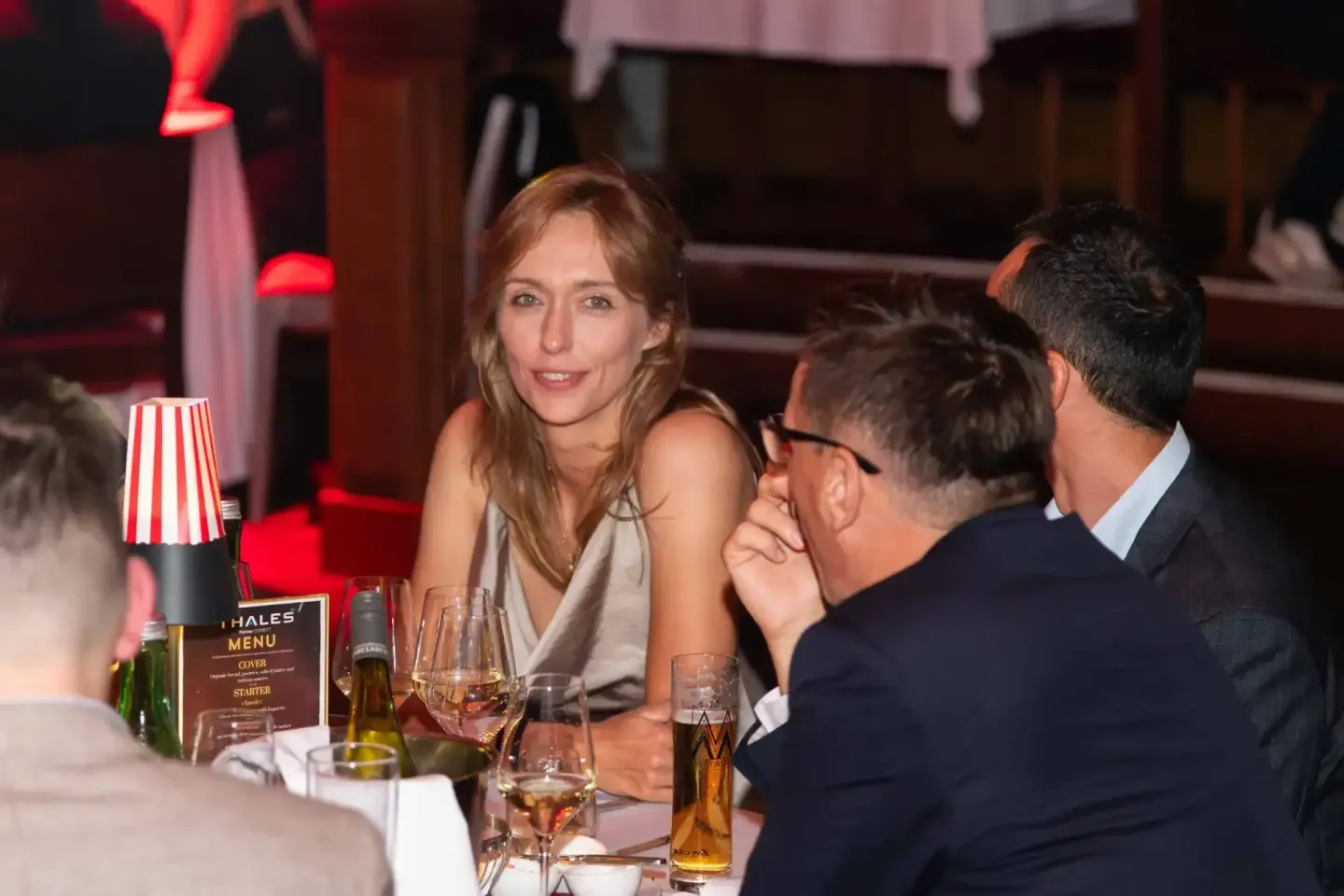 Elegantes Firmenevent Wien: Frau in Abendkleid im Gespräch mit Gästen am gedeckten Tisch mit Getränken und Thales Menü