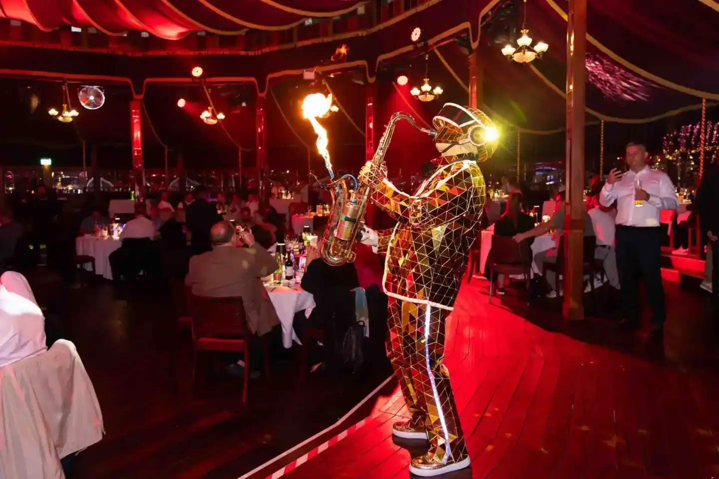 Beleuchtete Saxophon-Statue bei Gala-Dinner im roten Zirkuszelt mit Gästen an Tischen – Eventfotografie Wien