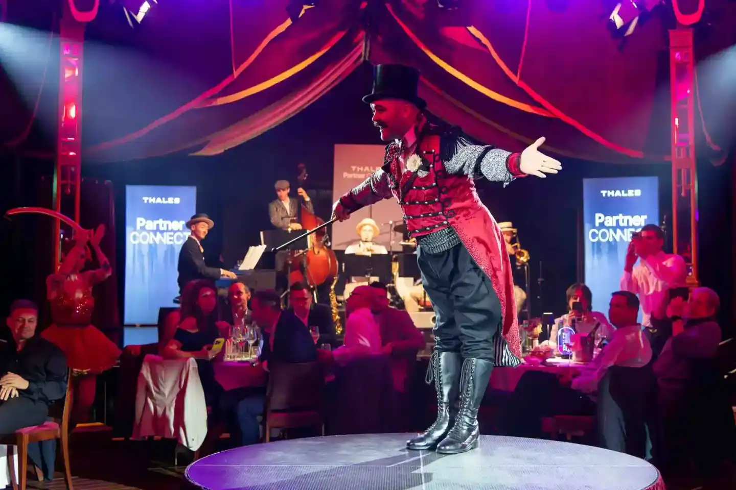 Zirkusartist in rotem Kostüm und Zylinder performt auf der Bühne beim Thales Partner Connect Event - Eventfotografie Wien