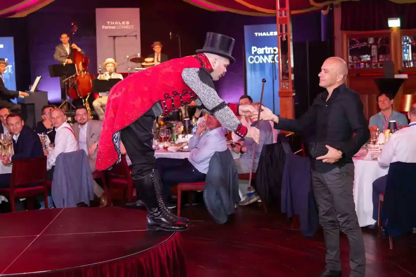 Showman in rotem Paillettenanzug und Zylinder performt bei Thales Partner Connect Firmenevent Wien vor Gästen an Tischen