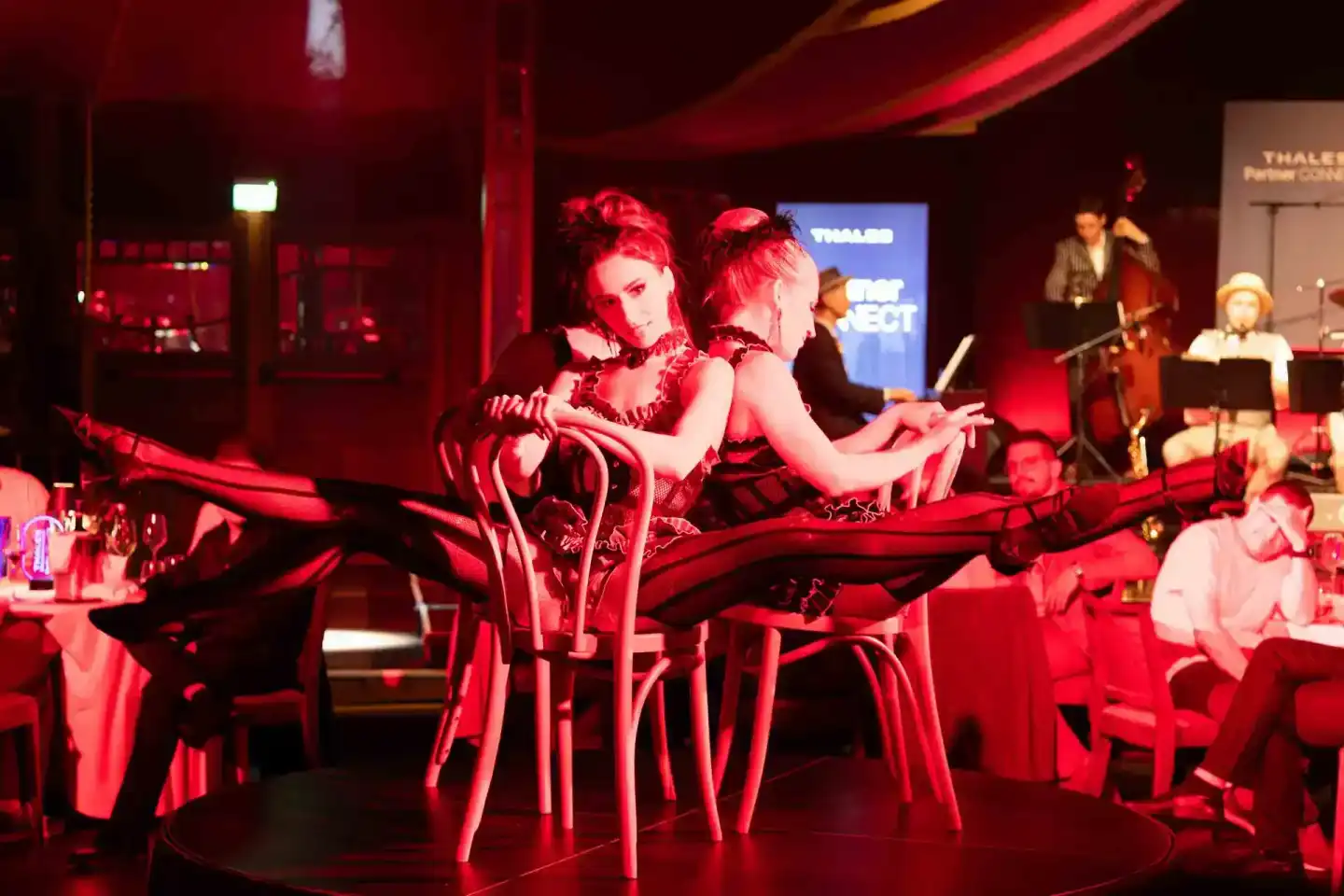 Zwei Performerinnen tanzen auf der Bühne beim Thales Firmenevent Wien unter roter Beleuchtung mit Live-Musikern im Hintergrun