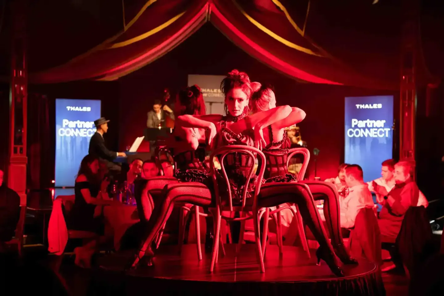 Eventfotograf dokumentiert Thales PartnerCONNECT Veranstaltung mit elegant gekleideten Personen an roten Stühlen unter rotem 