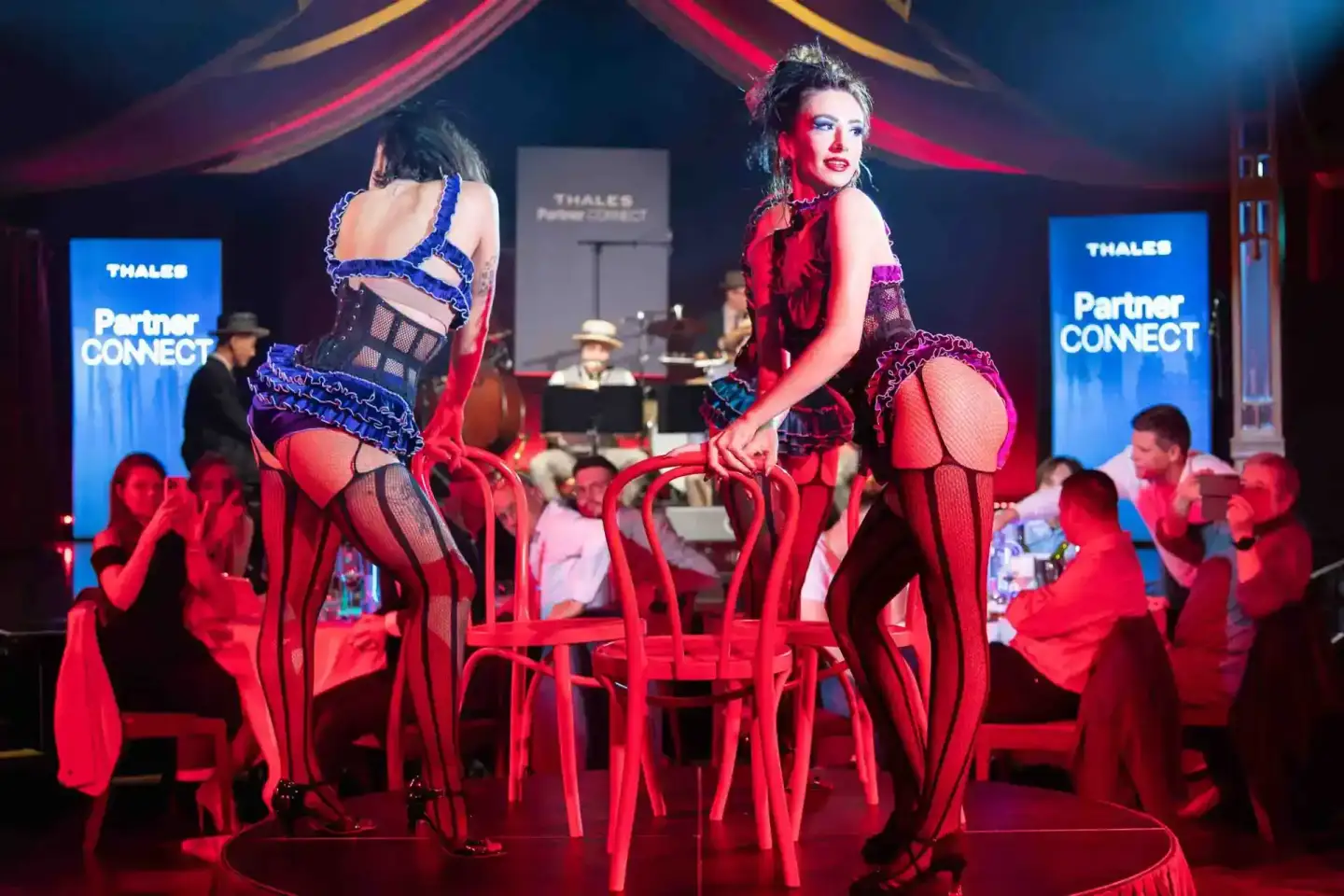 Zwei Performerinnen auf der Bühne beim Thales Partner Connect Event in Wien, umgeben von rotem Licht und Publikum
