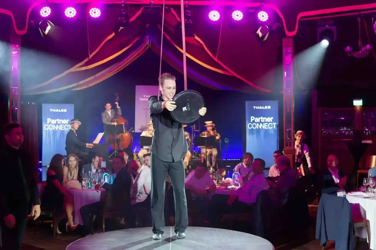Performer auf der Bühne beim Thales Partner Connect Event in Wien, hält eine schwarze Schale in die Höhe, umgeben von Gästen 