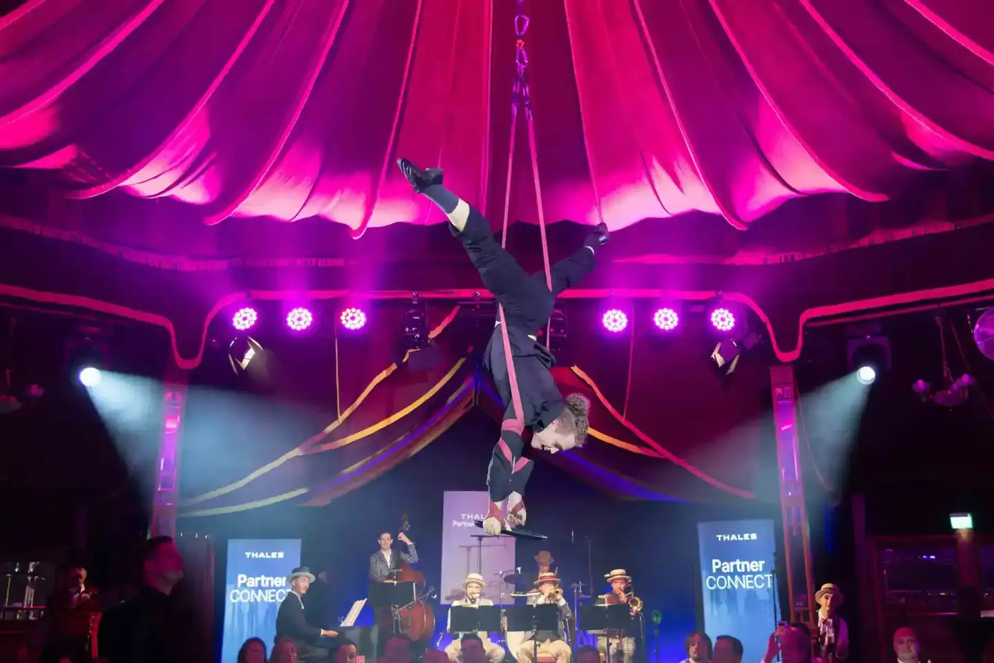Aerial Performer hängt kopfüber an Seilen über einer Bühne mit Live-Band bei Thales Partner Connect Event - Eventfotografie W