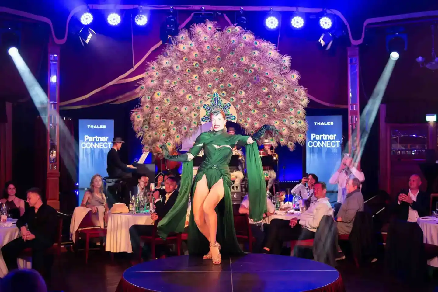 Performerin in grünem Kostüm mit großem Pfauenfeder-Kopfschmuck auf der Bühne während Thales Partner Connect Event Wien