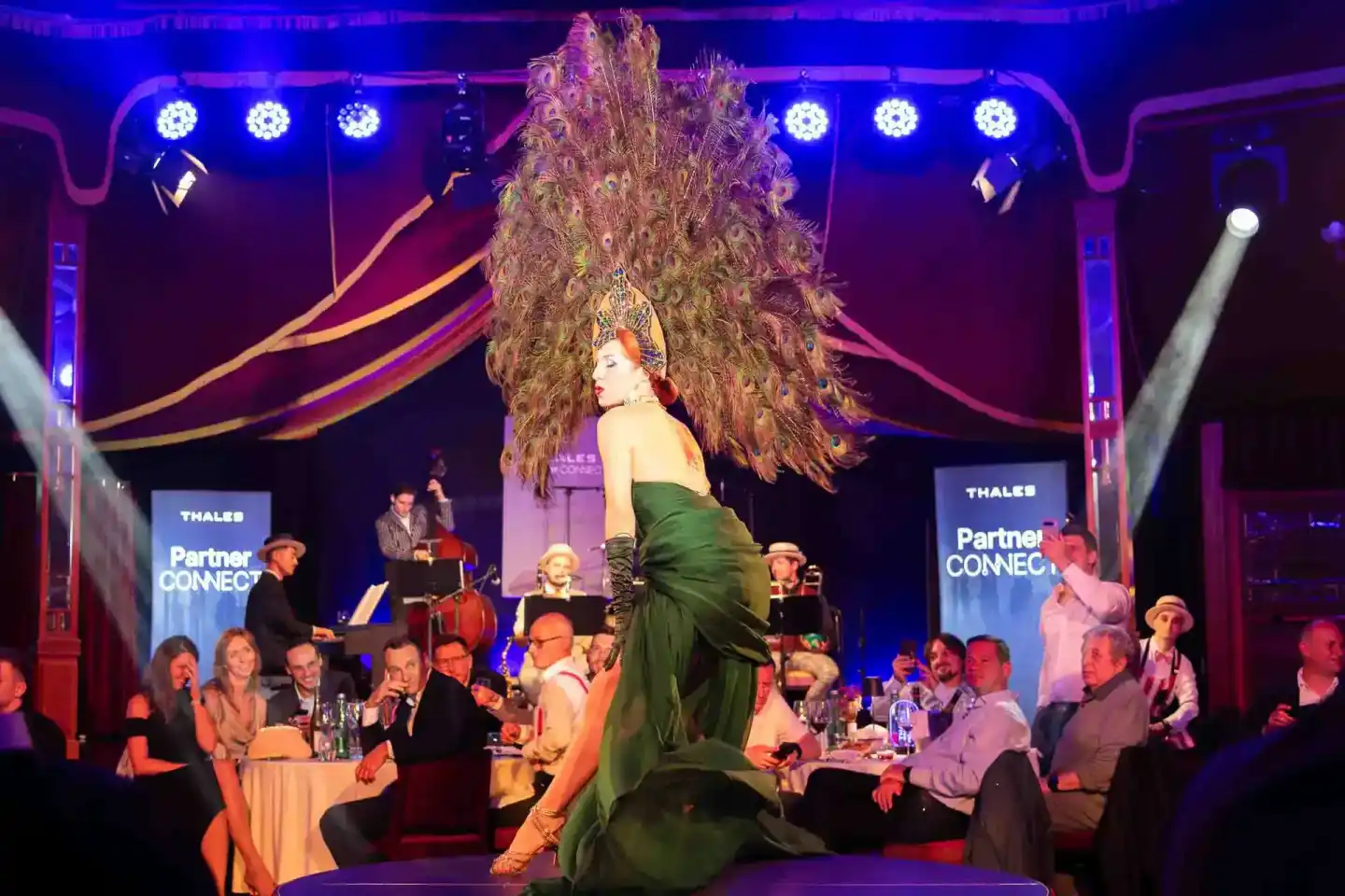 Elegante Künstlerin in grünem Kleid und Federkopfschmuck performt auf der Thales Partner Connect Gala vor sitzendem Publikum 