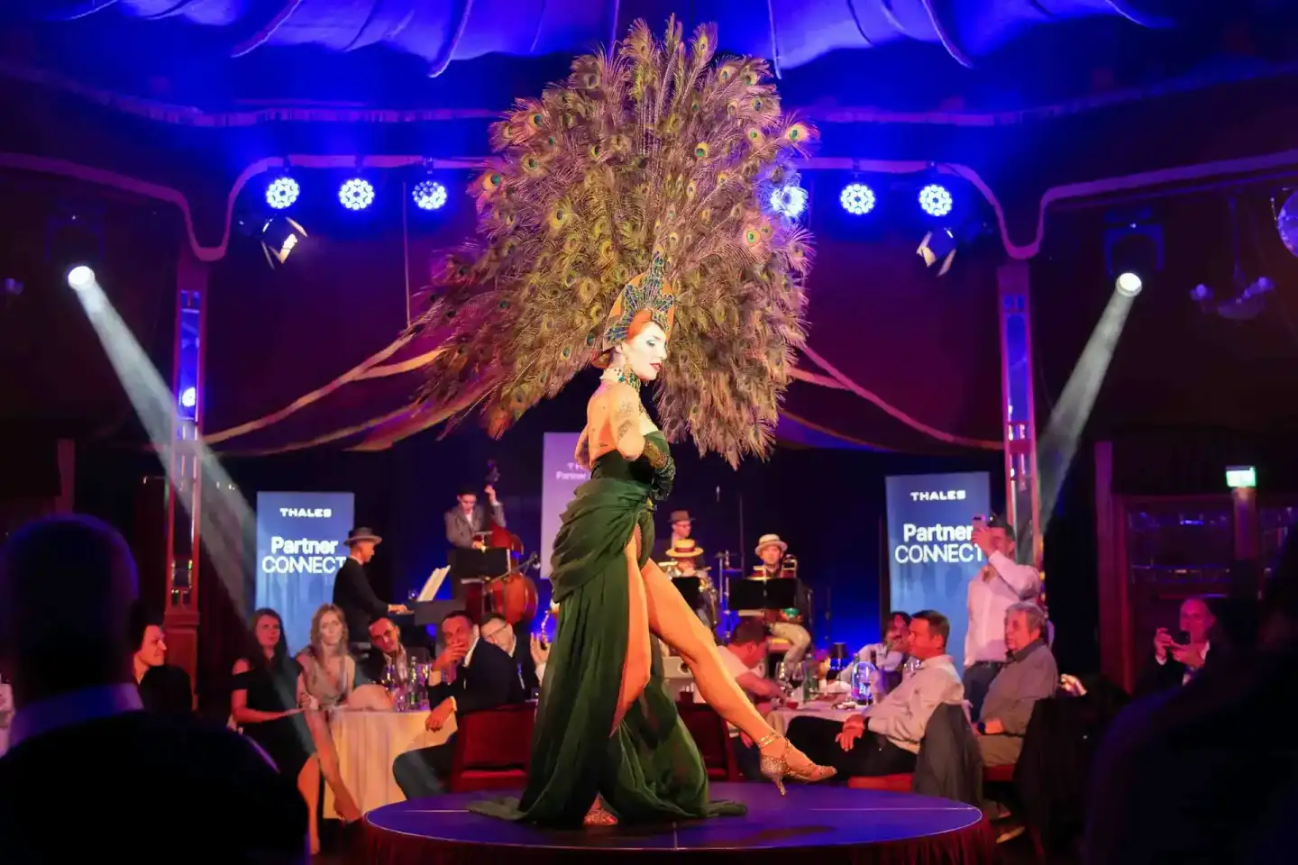 Elegante Performerin in grünem Kleid und großem Federkopfschmuck auf der Bühne während Thales Partner Connect Event - profess